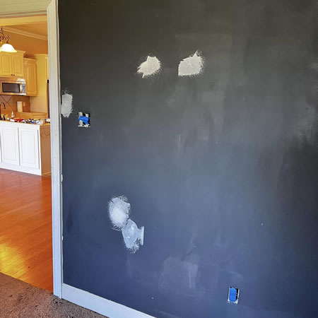 Painter masking trim and repairing drywall in a prairieville living room before painting